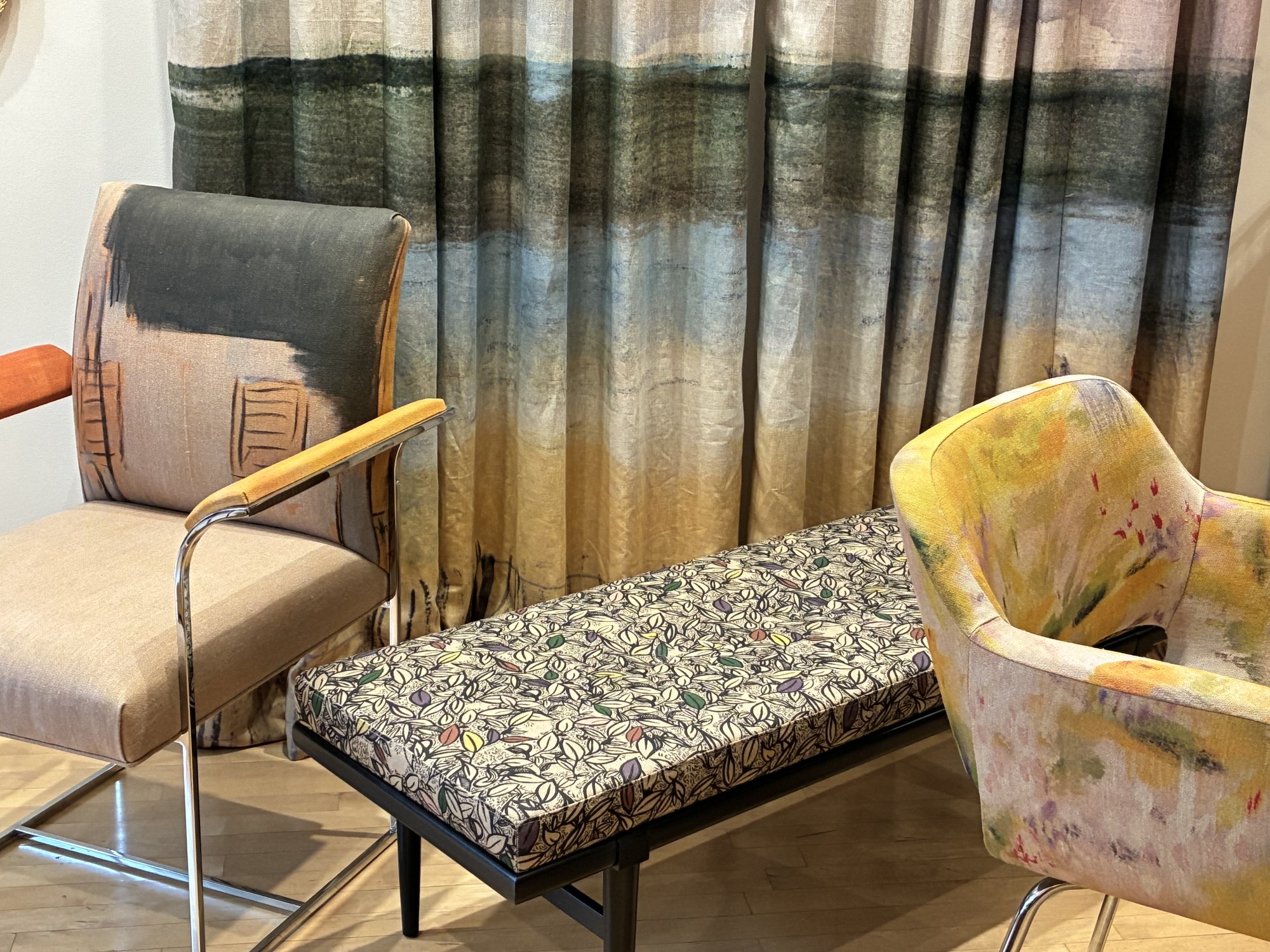 Upholstered bench and two armchairs in painterly fabrics against a landscape-print curtain